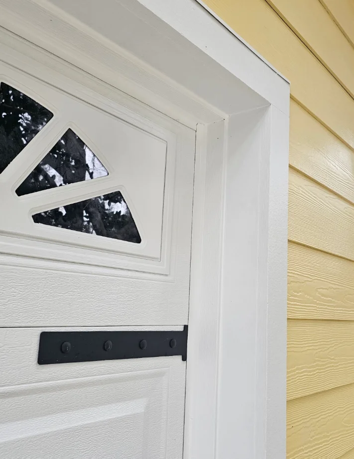 White entry door with fan-shaped glass transom and black strap hinge beside white trim and yellow horizontal lap siding