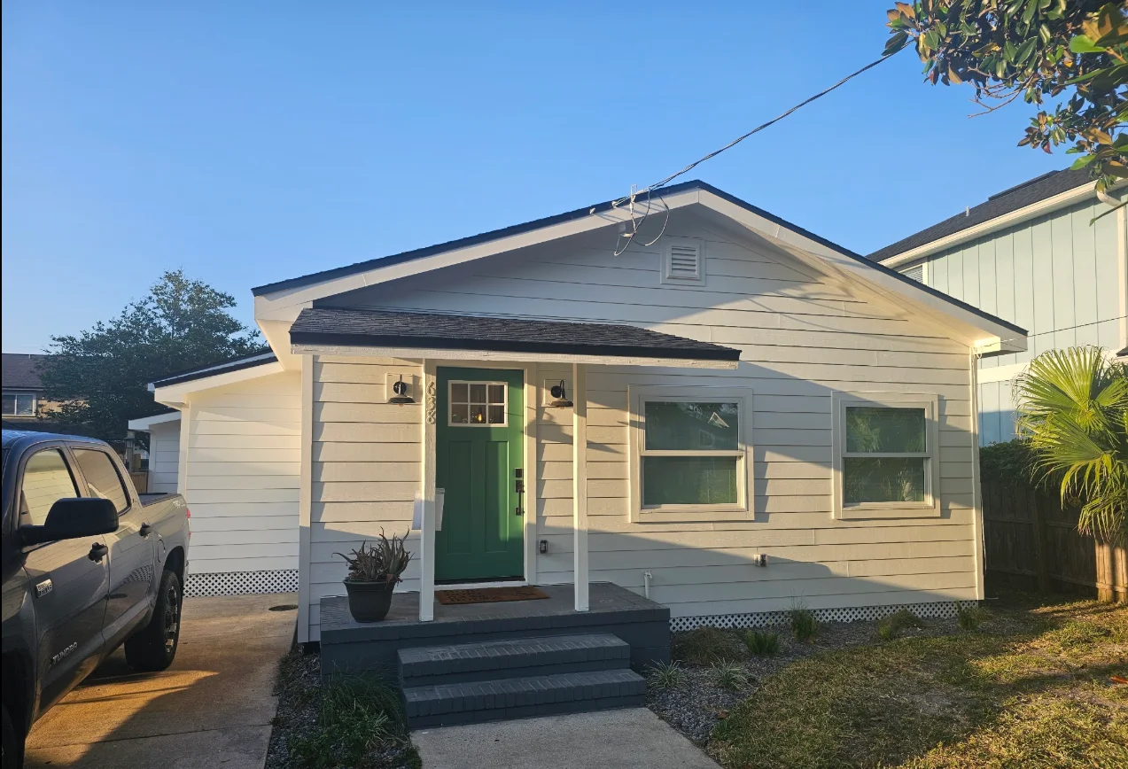 White horizontal lap siding with white trim and lattice skirting on a cottage with a green front door and dark porch canopy