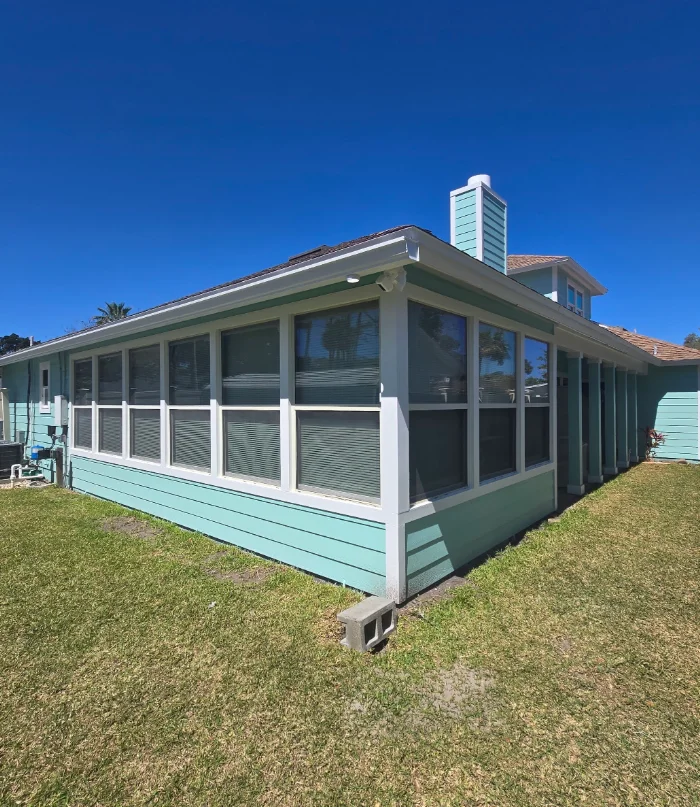 Teal horizontal lap siding and white-framed windows on a sunroom addition with white trim and fascia