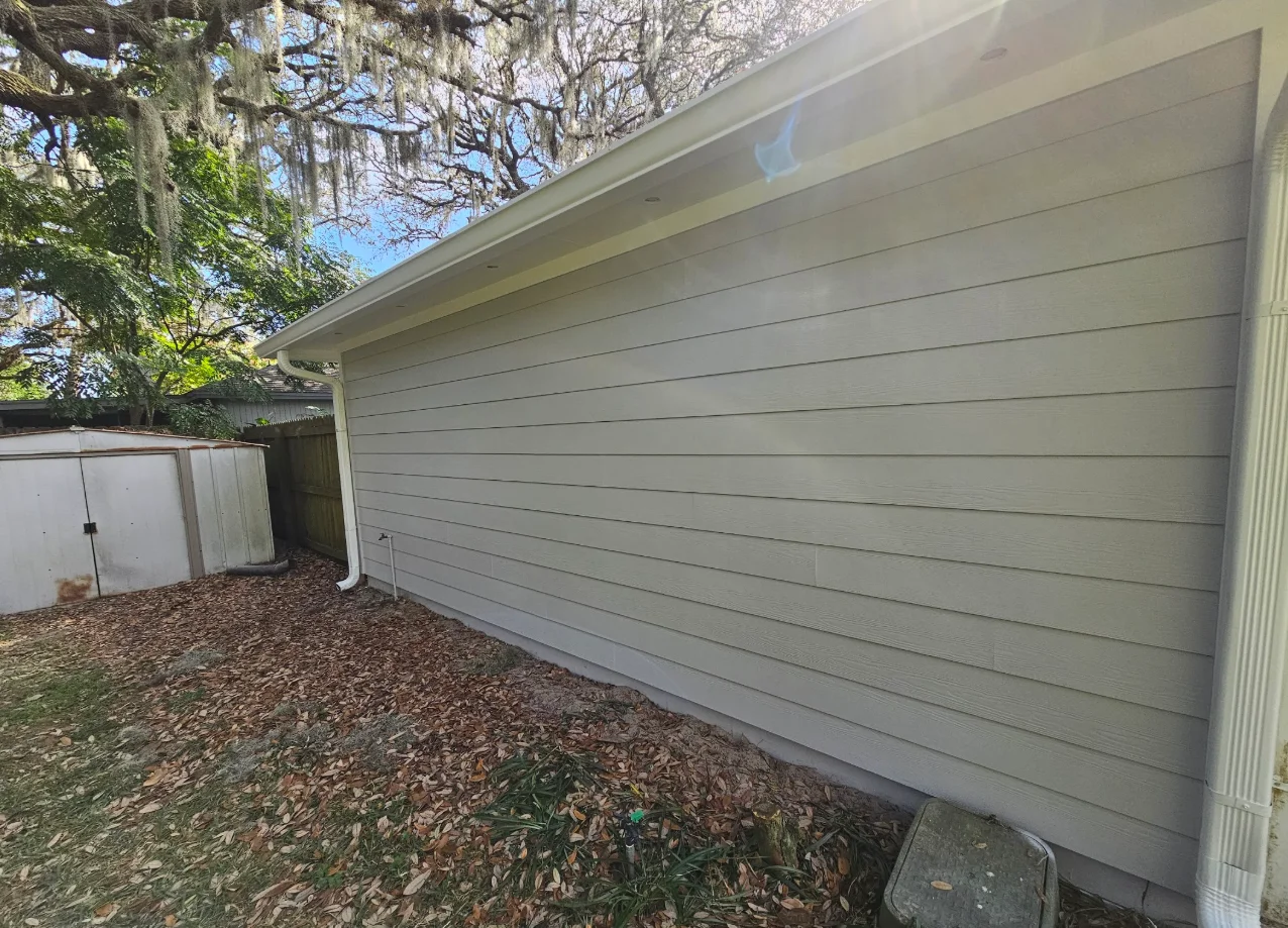 Light gray horizontal lap siding with wood-grain texture on a single-story wall, white fascia, soffit, and downspout