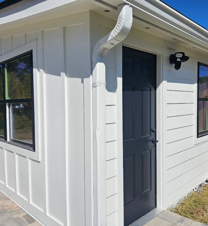 White board-and-batten and horizontal lap siding with dark gray entry door, black-framed windows, and white gutter downspout
