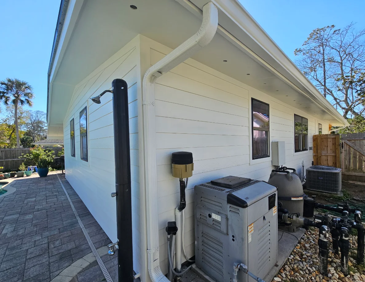 White horizontal lap siding with white downspout, dark-framed windows, and soffit lighting on a single-story home