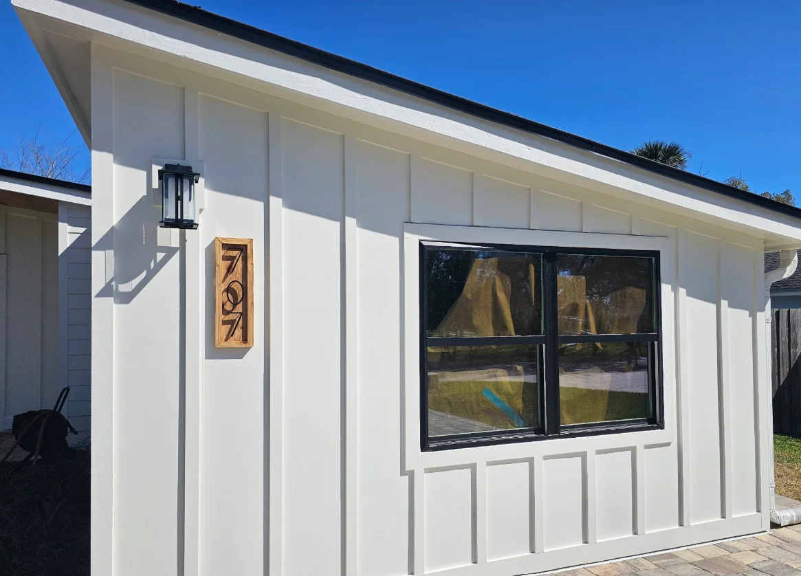 White board-and-batten siding with black-framed window, wood house number plaque, and black wall lantern