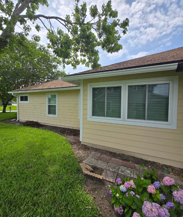 Single-story home with pale yellow horizontal lap siding, white trim, and white-framed windows beside a brown shingle roof