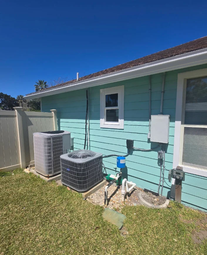 Teal horizontal lap siding with white window trim and outdoor AC condenser units beside a tan vinyl fence