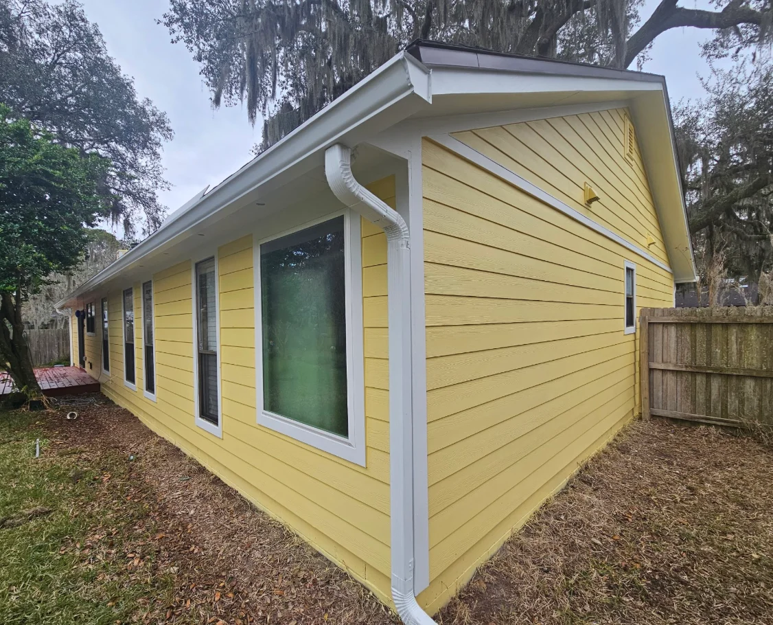 Yellow horizontal lap siding with white window trim, corner trim, and white gutter and downspout on a single-story home