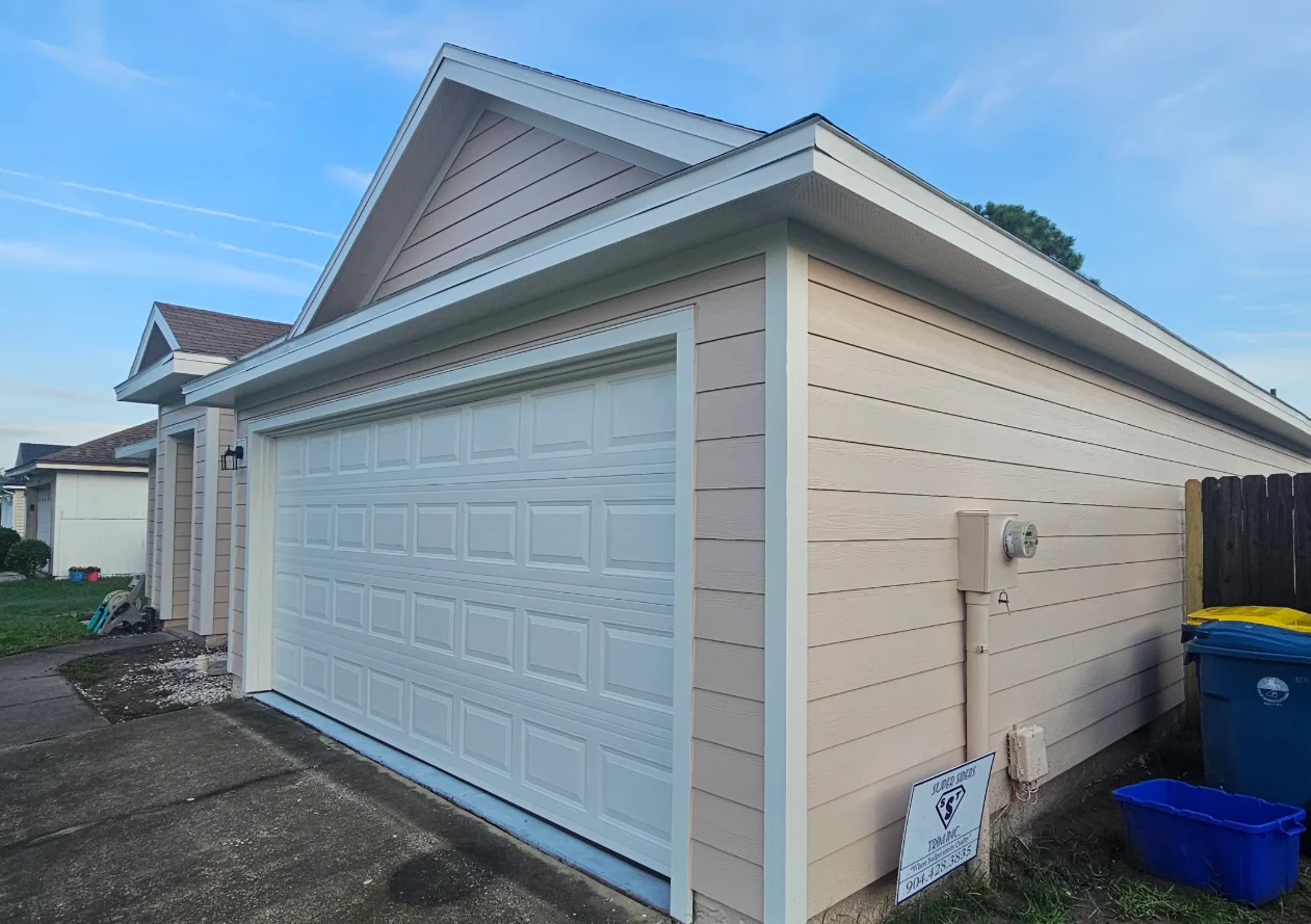 Tan horizontal lap siding with white trim and raised-panel white garage door on a single-story garage