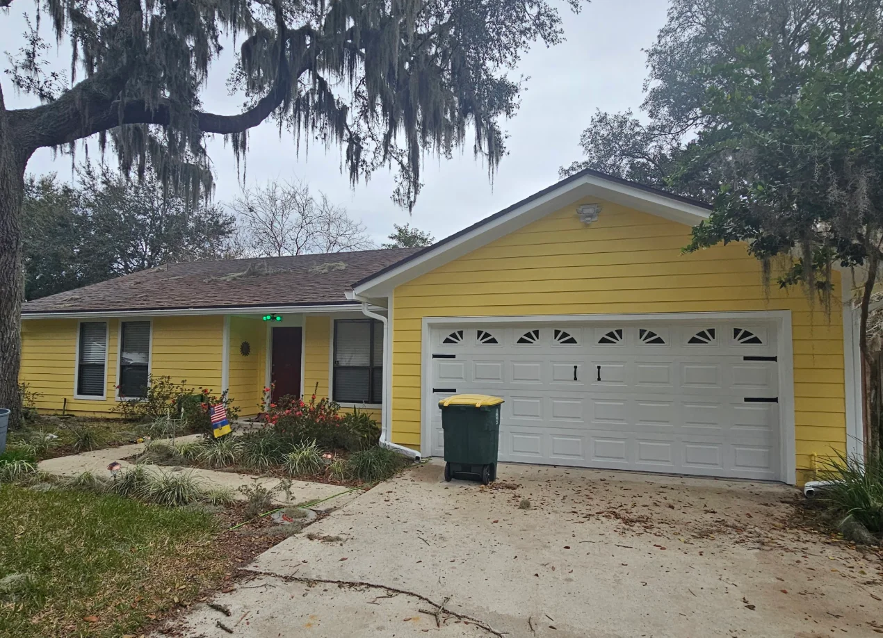 Yellow horizontal lap siding with white trim, corners, and soffit on a single-story house with white arched-window garage door