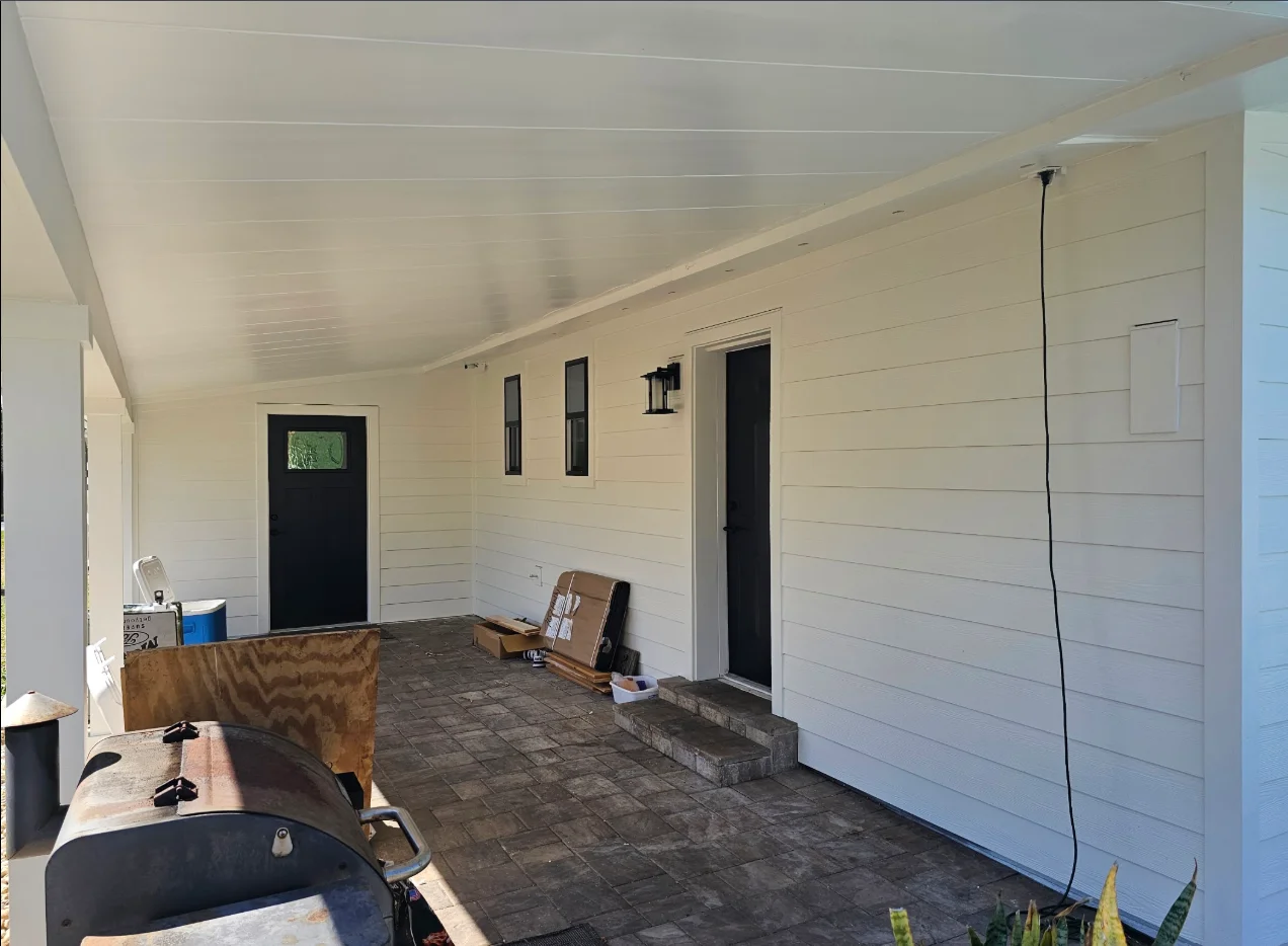 Cream horizontal lap siding with white trim, black doors and windows, and white paneled soffit on a covered patio