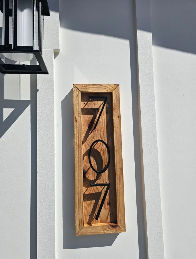 Wood-framed address plaque with black metal 707 numerals mounted on white stucco wall