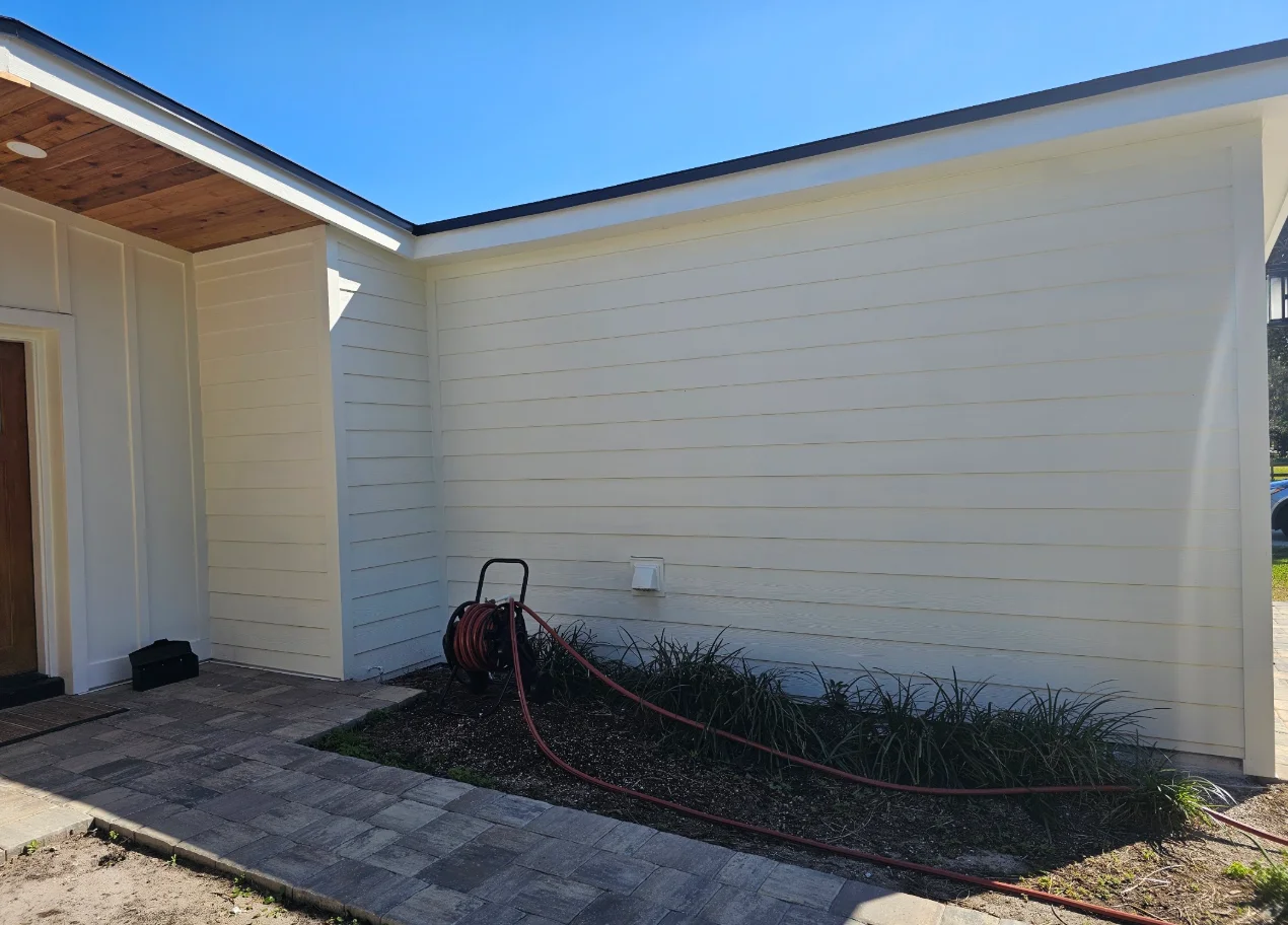 Cream horizontal lap siding with board-and-batten trim panels, dark metal roof edge, and wood soffit on a single-story home