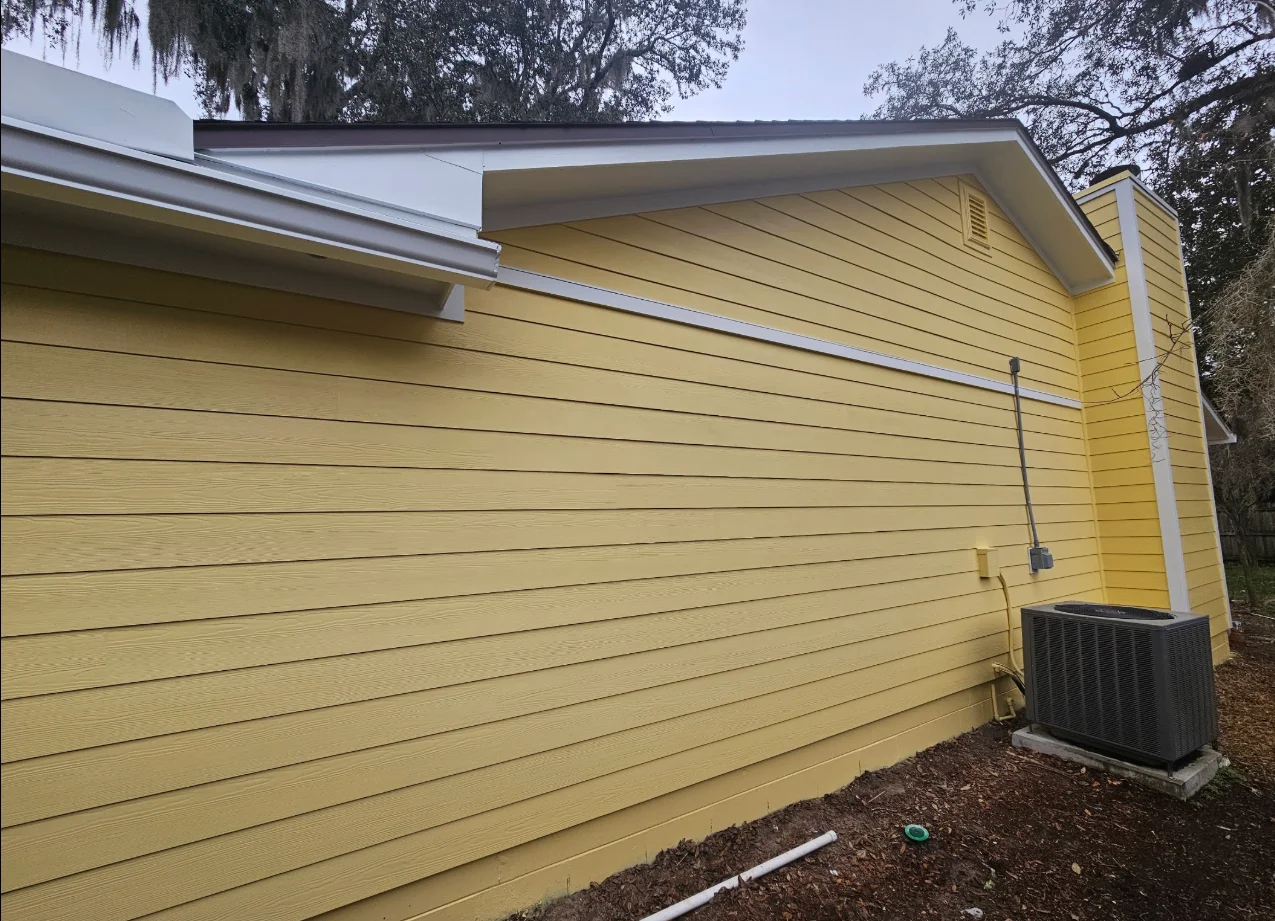 Yellow horizontal lap siding with white trim, corner boards, and fascia on a single-story home beside a gray AC unit